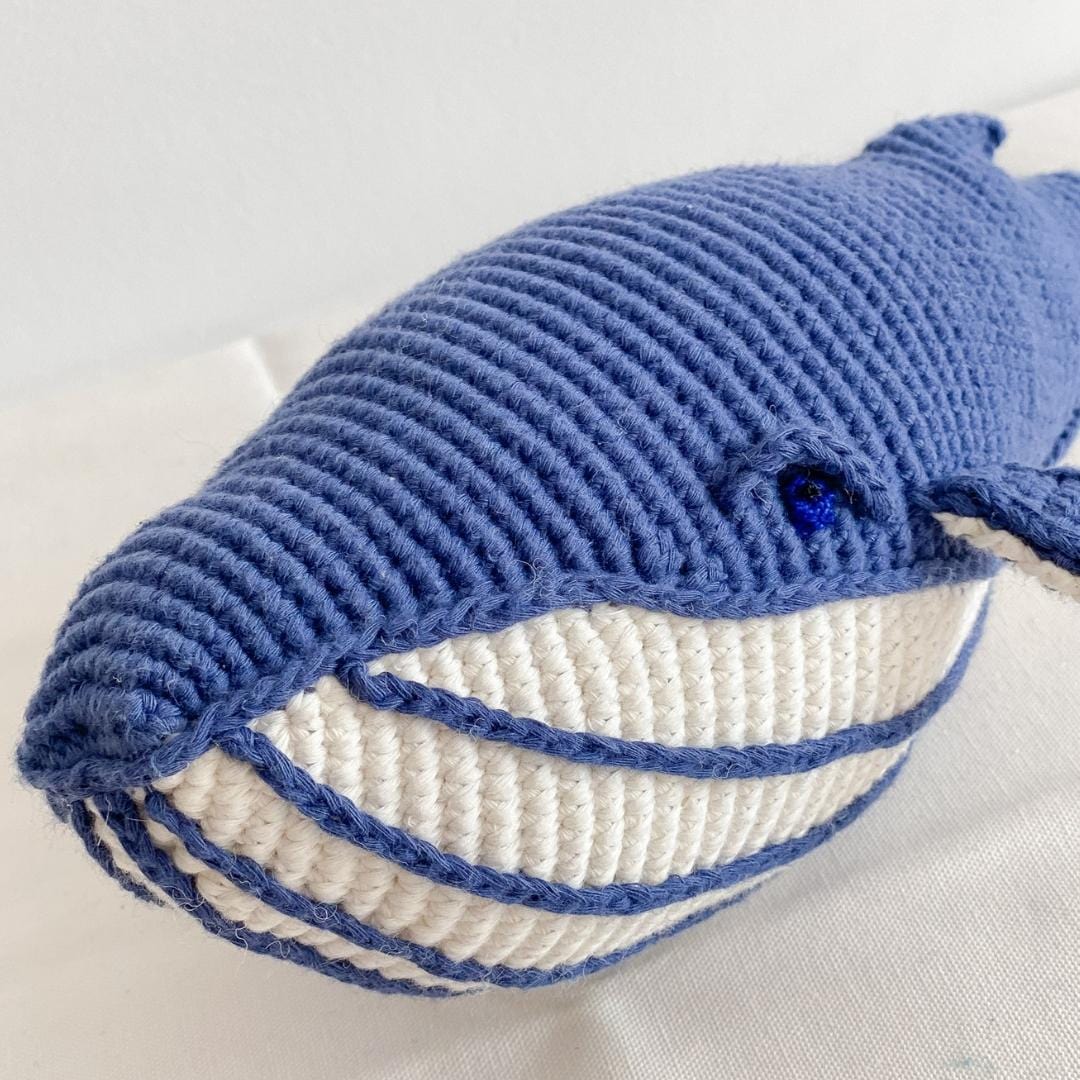 Close-up of crocheted whale plush with a blue eye and cream, blue-striped belly.