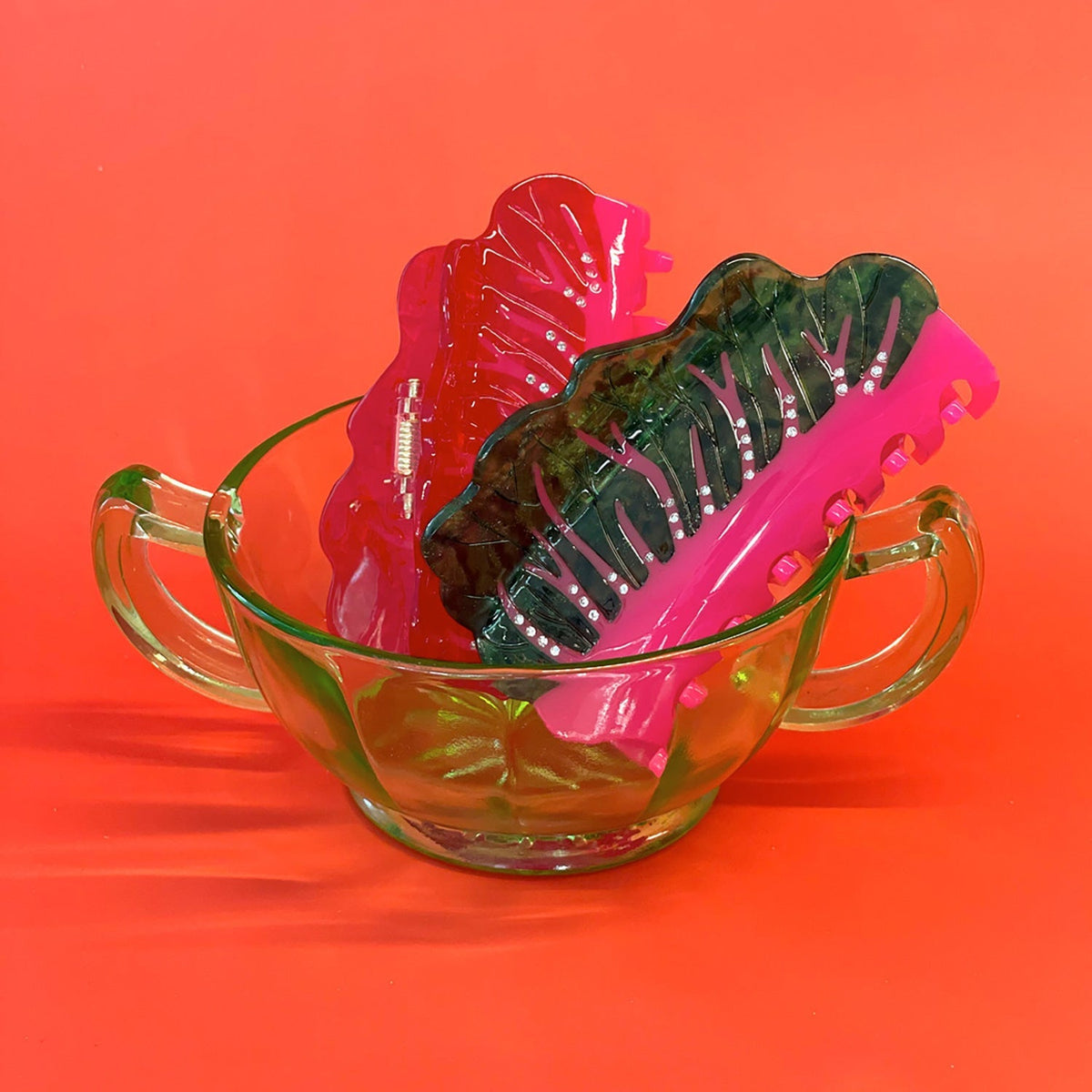 Hair claw with clear green body, red insert, pink underside, and metal hinge bar
