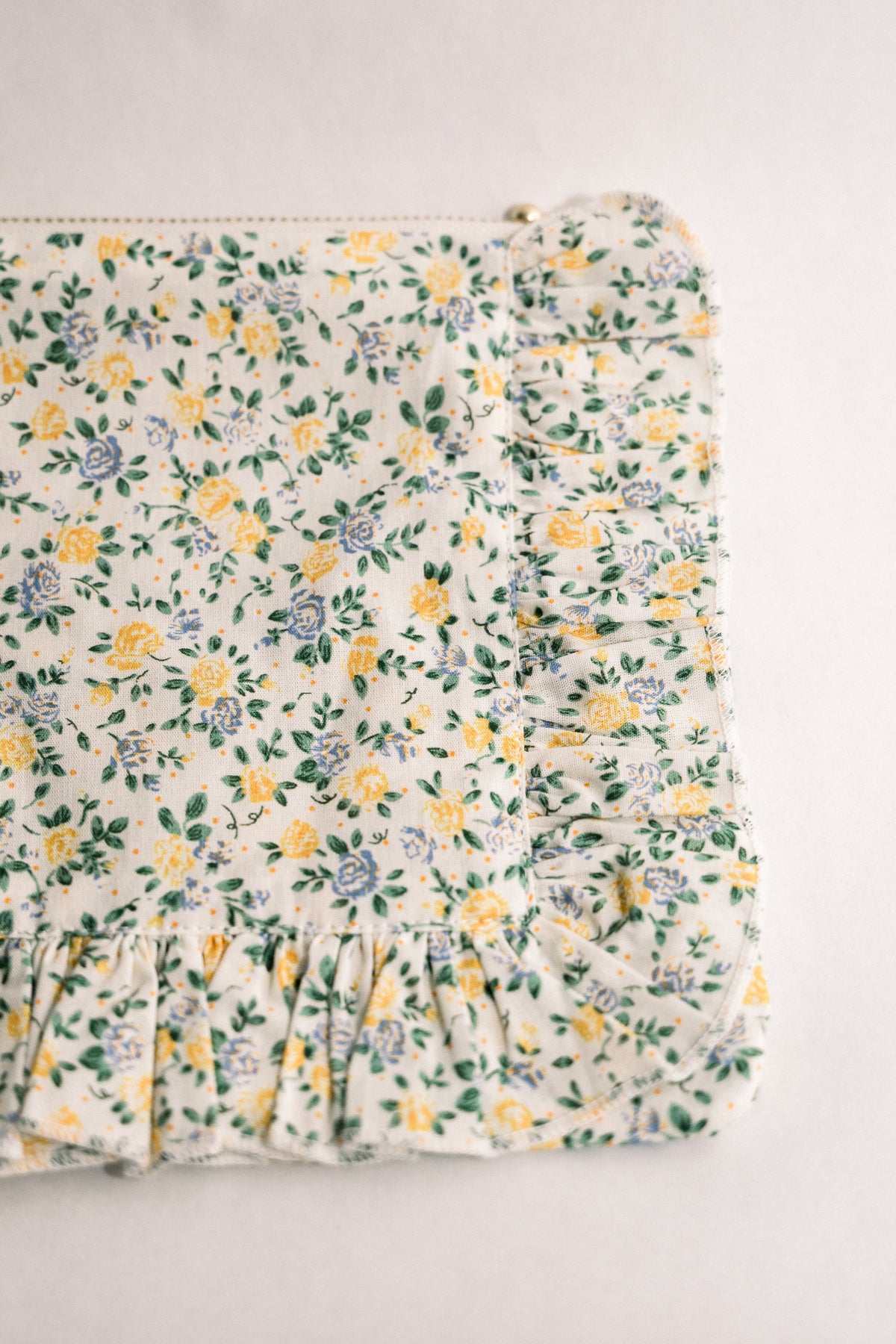 Floral ruffle zipper pouch detail view, gathered trim and zipper along side edge.