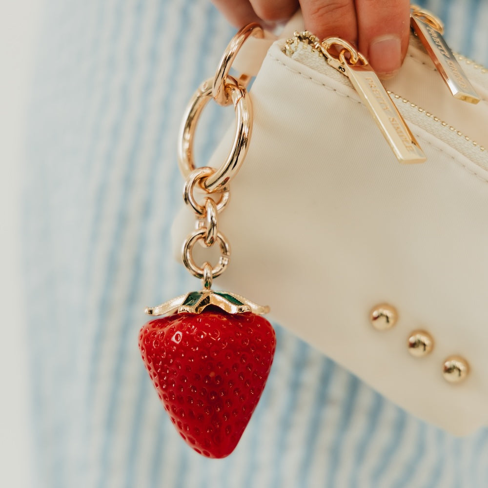 Red strawberry bag charm with gold chain and green leaf, attached to a bag