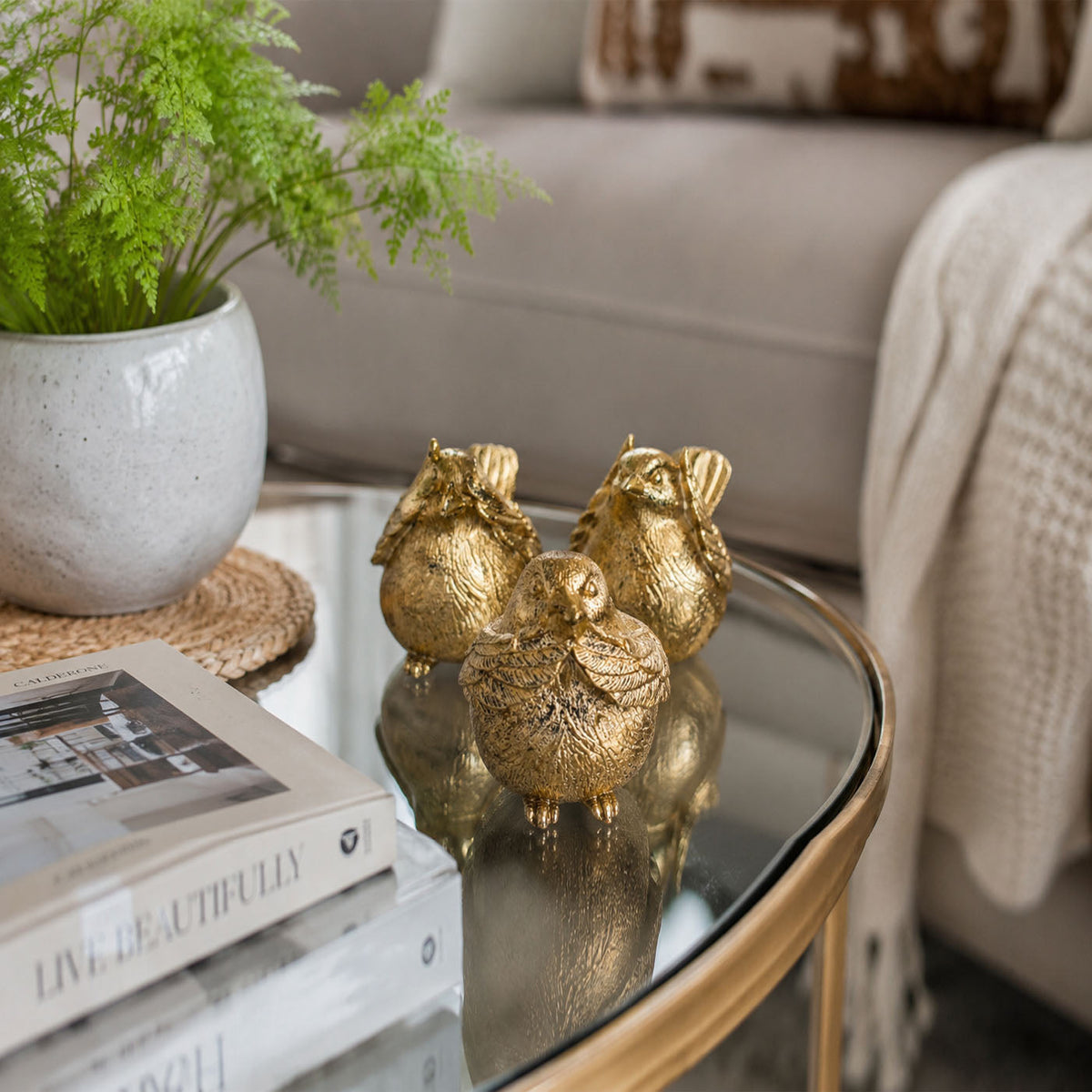 Gold-tone three bird figurines clustered together on a glass table