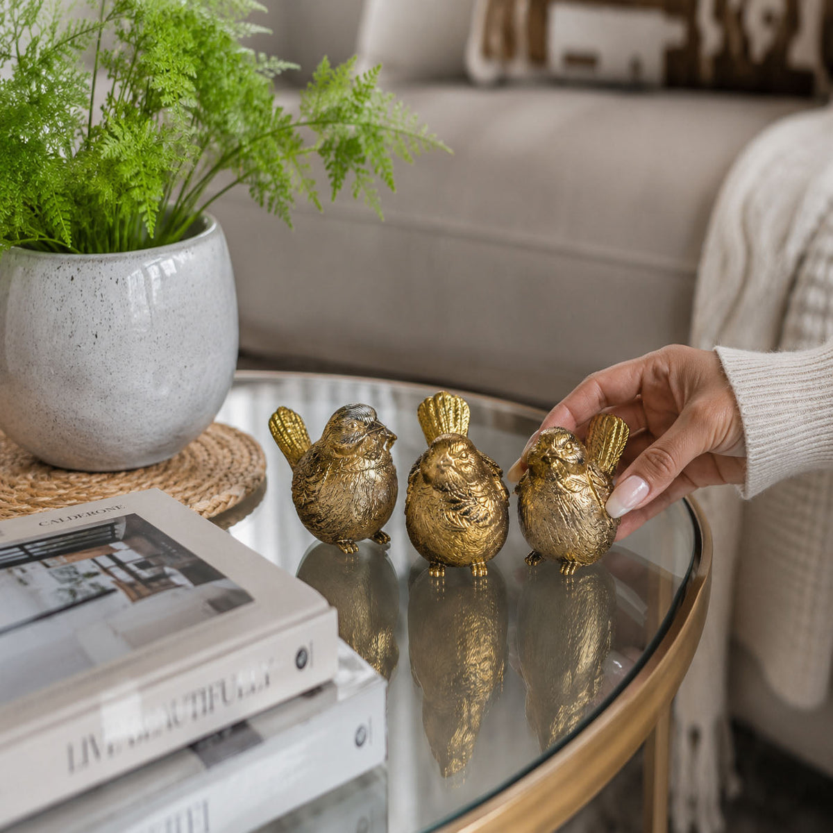 Three gold-tone bird figurines on a tray, hand adjusting one