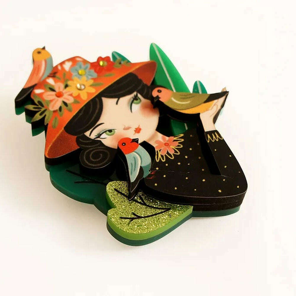 Bird lover brooch featuring illustrated woman in hat with birds, glittery green edges