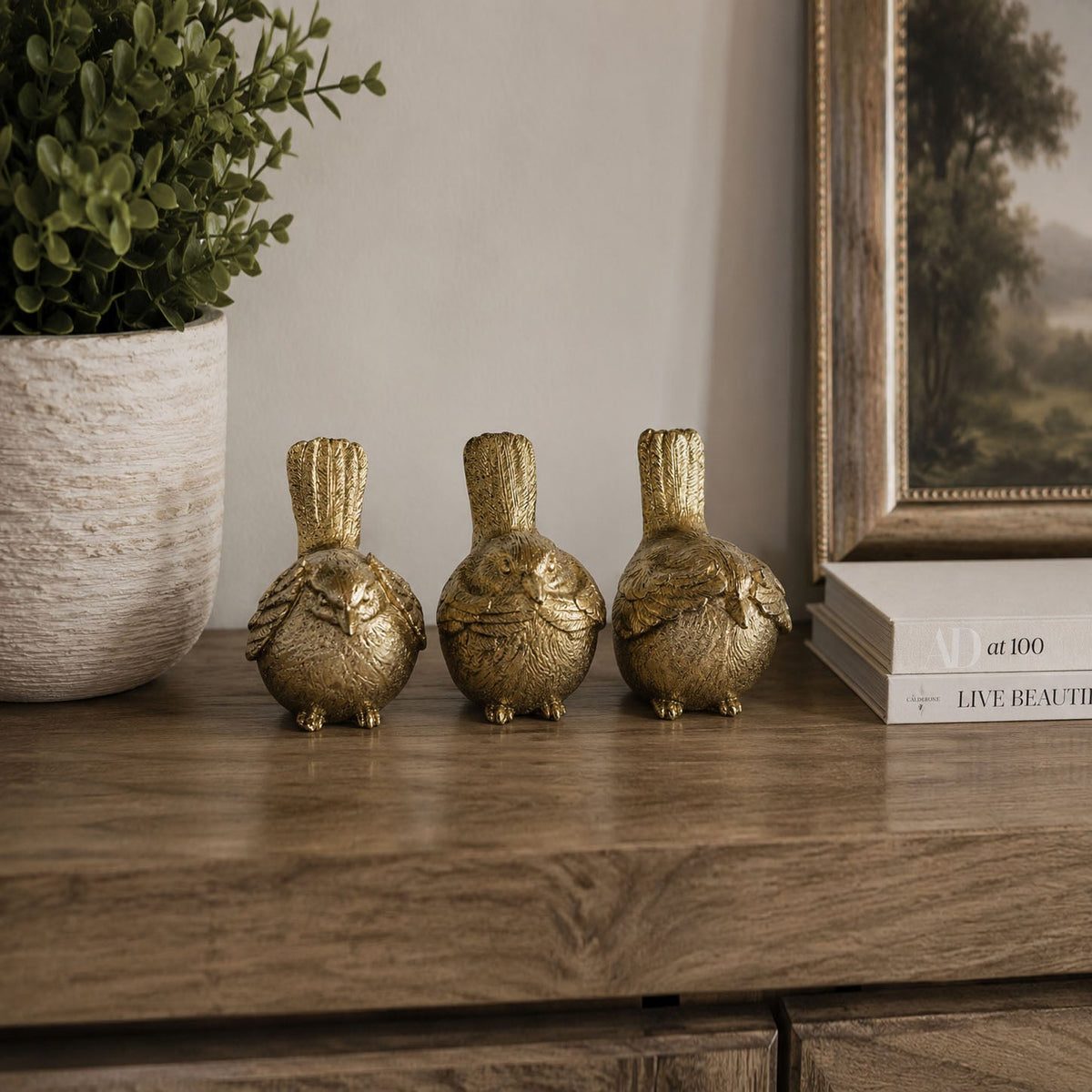 Three small gold-tone bird figurines displayed on a dark wooden shelf