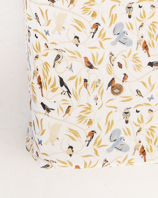 White crib sheet with colorful birds and leaves pattern, fitted corner visible