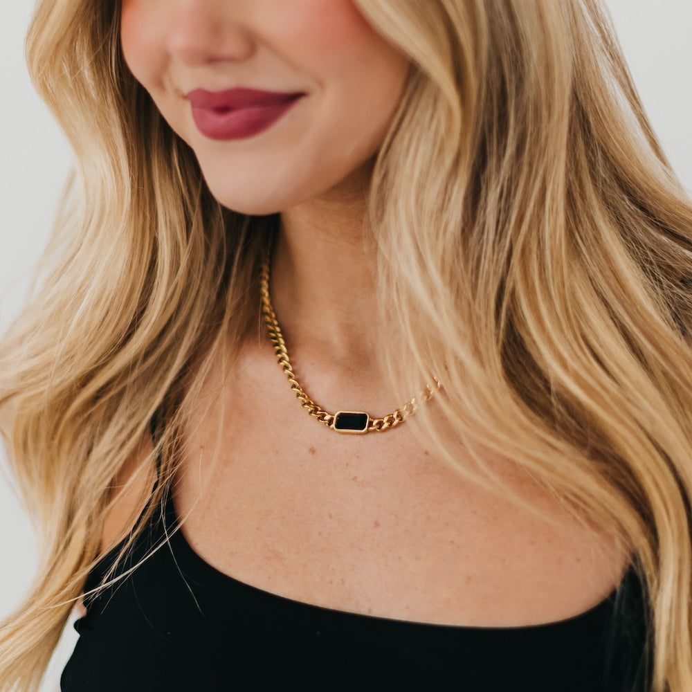 Gold chain necklace with black rectangular pendant at the neckline