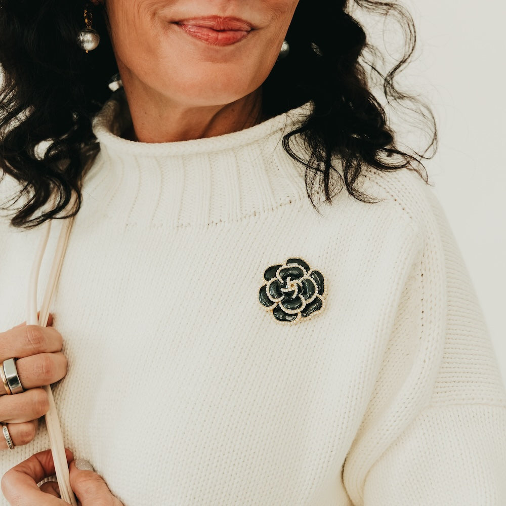 Black flower brooch with pearl trim, pinned to a cream knit top