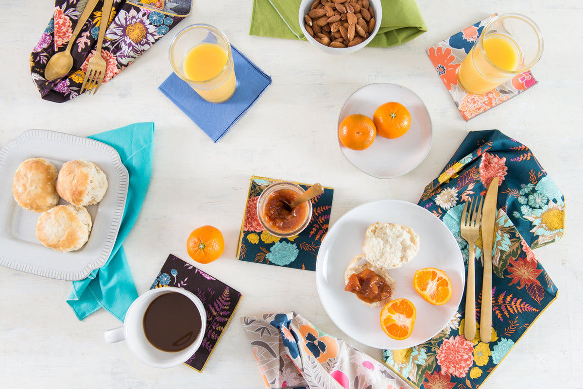 Four floral cloth napkins in navy, teal, orange, and yellow laid across tabletop