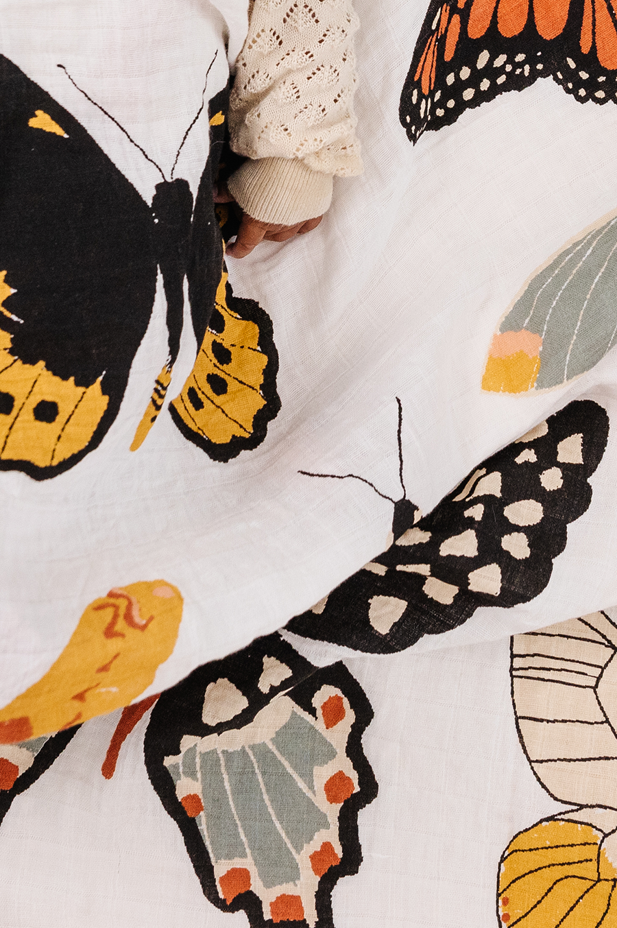 White muslin swaddle fabric close-up with black, orange, and yellow butterfly and moth print