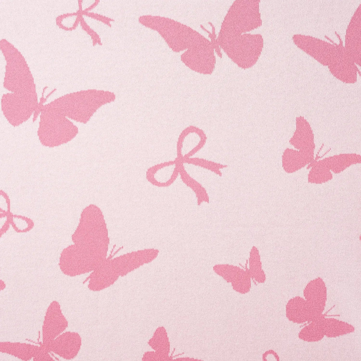 Pink knit blanket close-up showing white butterflies, bows, and jacquard texture.
