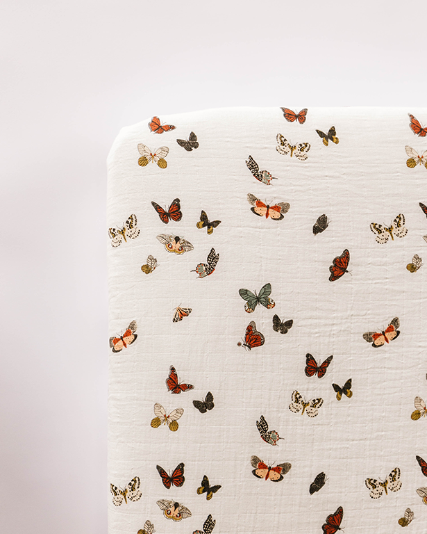 Off-white crib sheet with colorful butterfly pattern and small leaf details