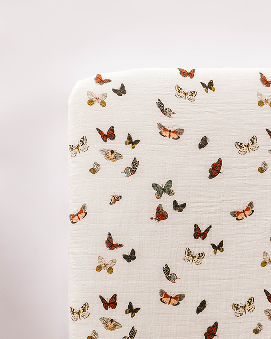 Off-white crib sheet with colorful butterfly pattern and small leaf details