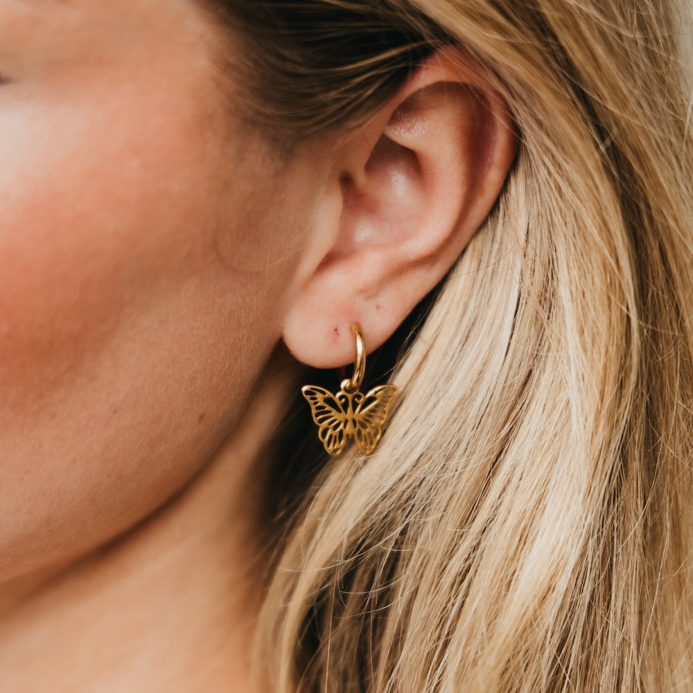Gold butterfly drop huggie earrings with butterfly charm, worn on ear