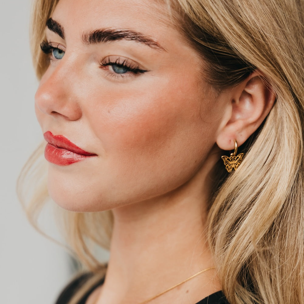 Butterfly drop huggie earrings with gold butterfly charm, worn on ear