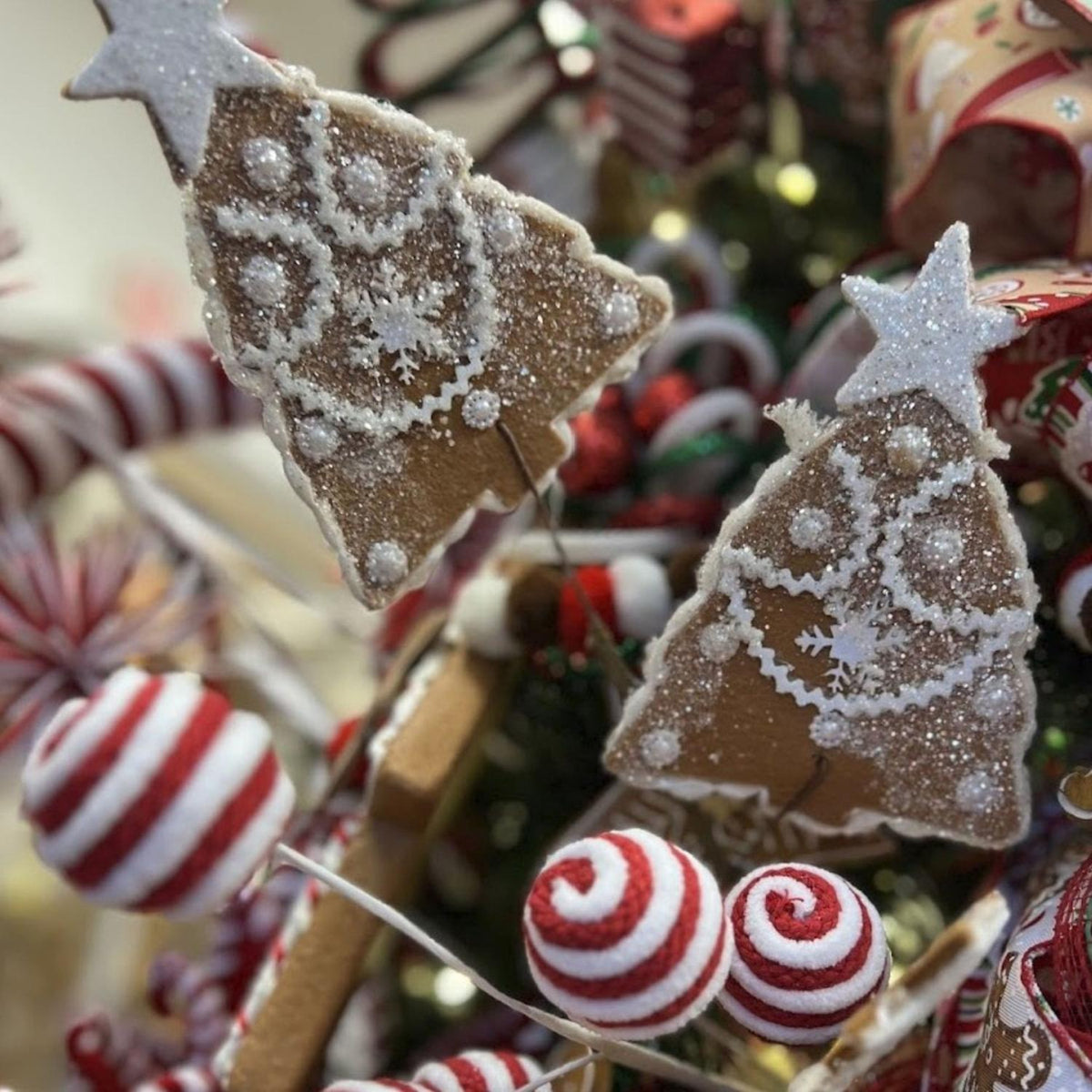 Two gingerbread Christmas ornaments with white snowflake patterns and star toppers on stems