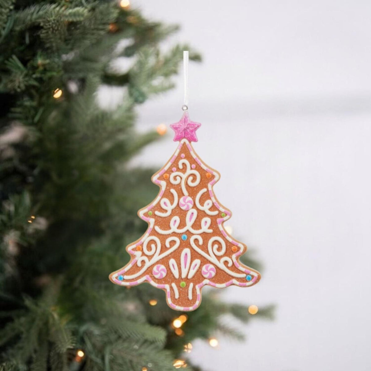 Gingerbread tree ornament hanging from cord, orange-brown with pink and white icing