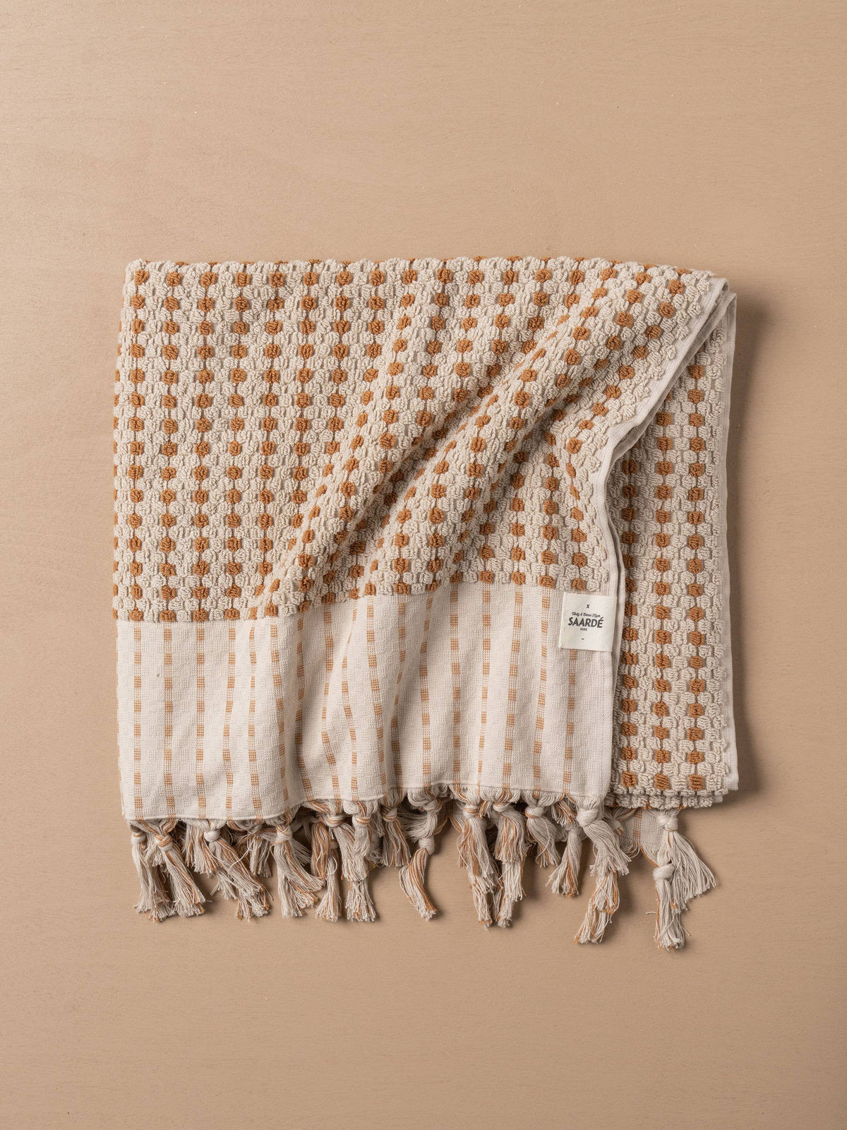 Turkish hand towel folded with terracotta grid and stone stripes, visible woven edge tassels
