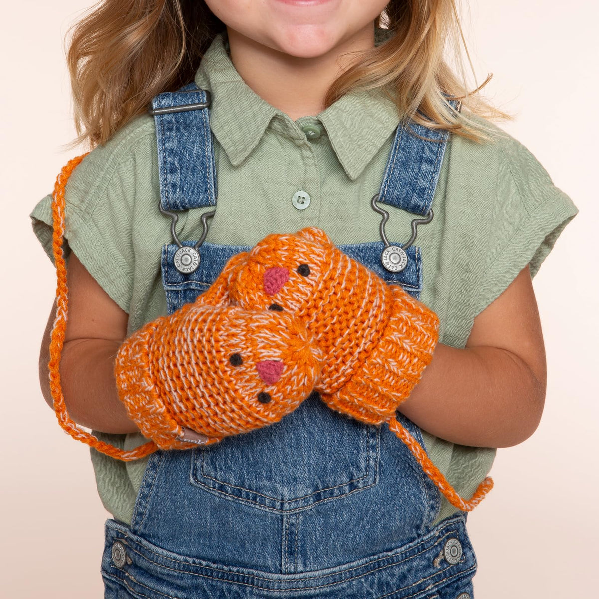 Child wearing rusty orange chick mittens with a connecting cord