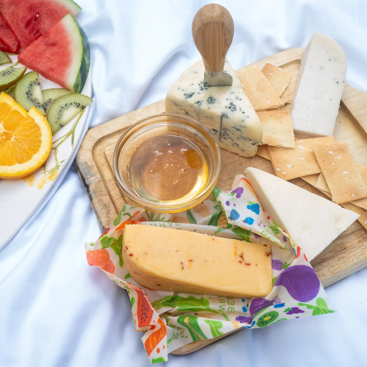 Reusable food wraps with assorted fruit pattern, folded around cheese and bread