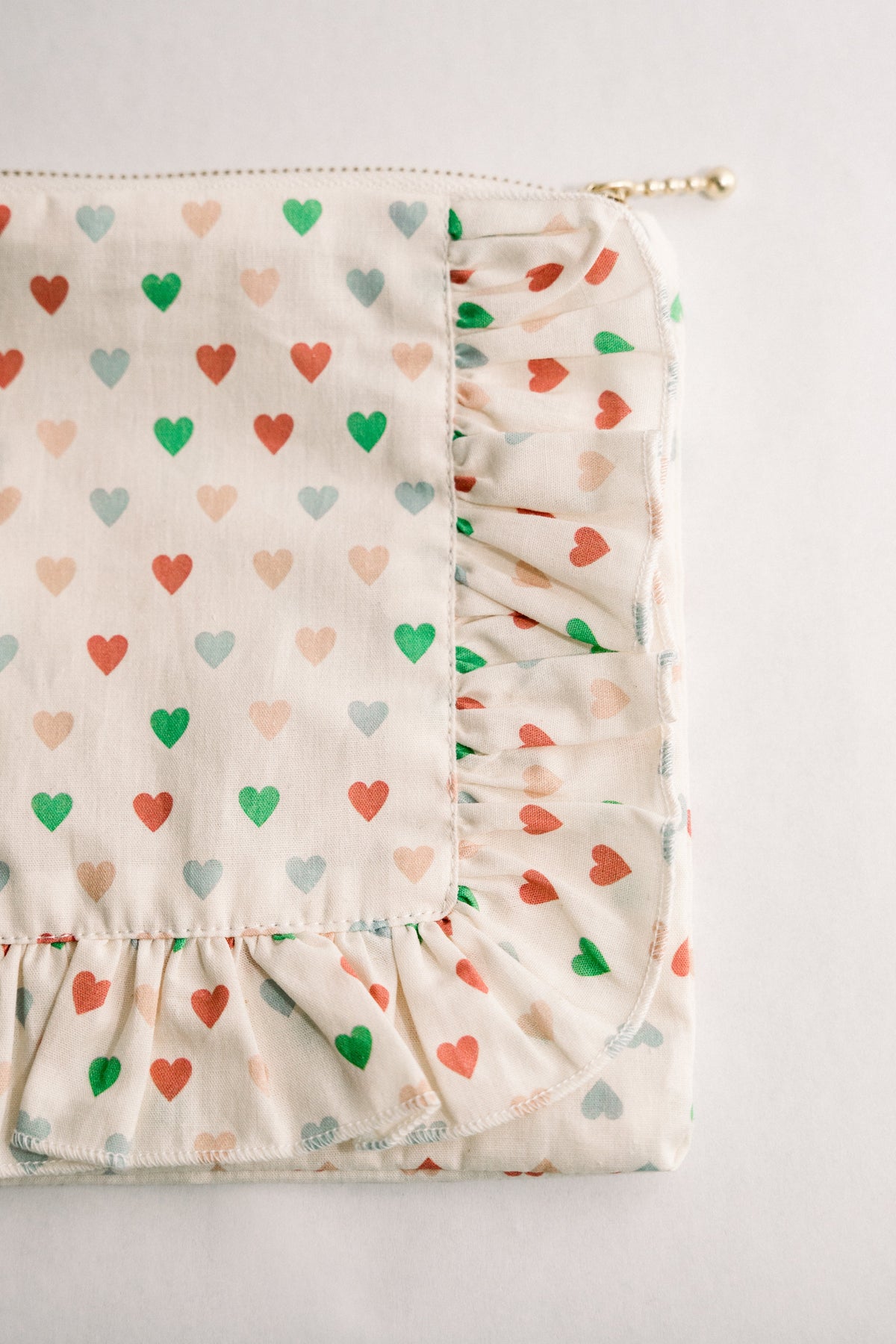 White heart-print ruffle zipper pouch with gold zipper pull