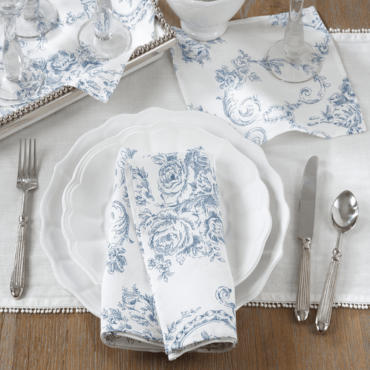 Set of 4 white linen napkins with blue floral toile print, folded on a white plate