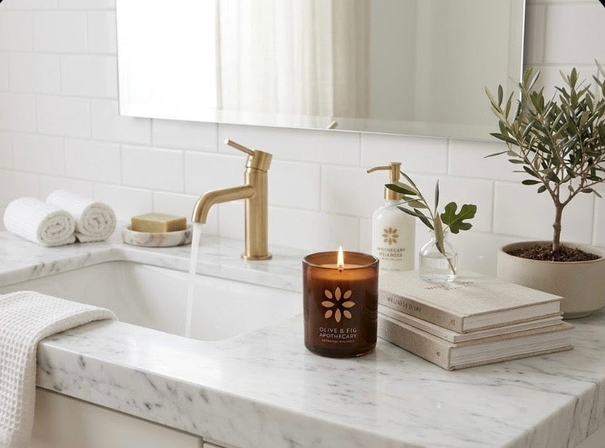 Amber jar candle on marble vanity among soap bars, plants, and books