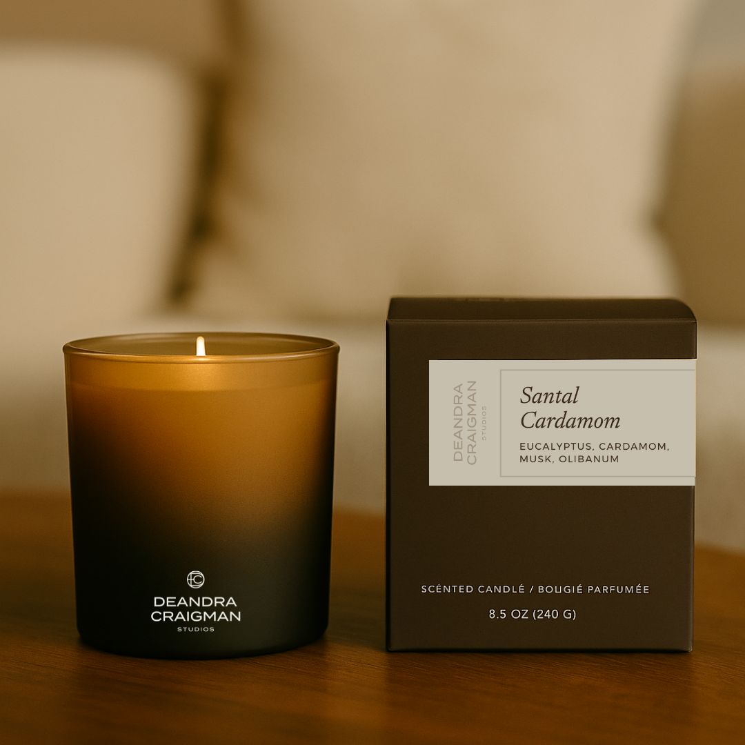 Scented candle and product box on a wooden surface, Deandra Craigman logo visible