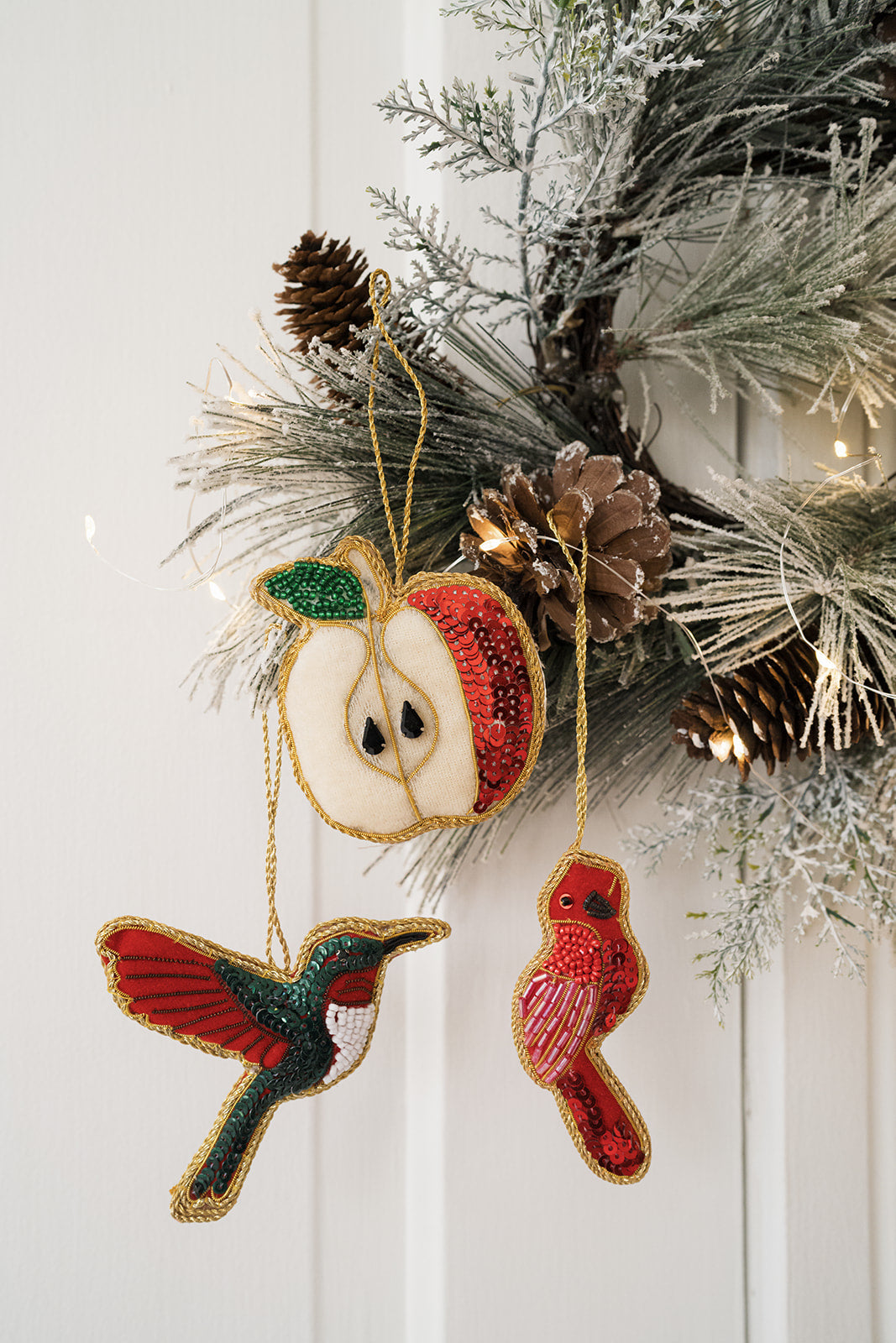 Plush hummingbird ornament with beaded wings hanging on pine garland with other figures