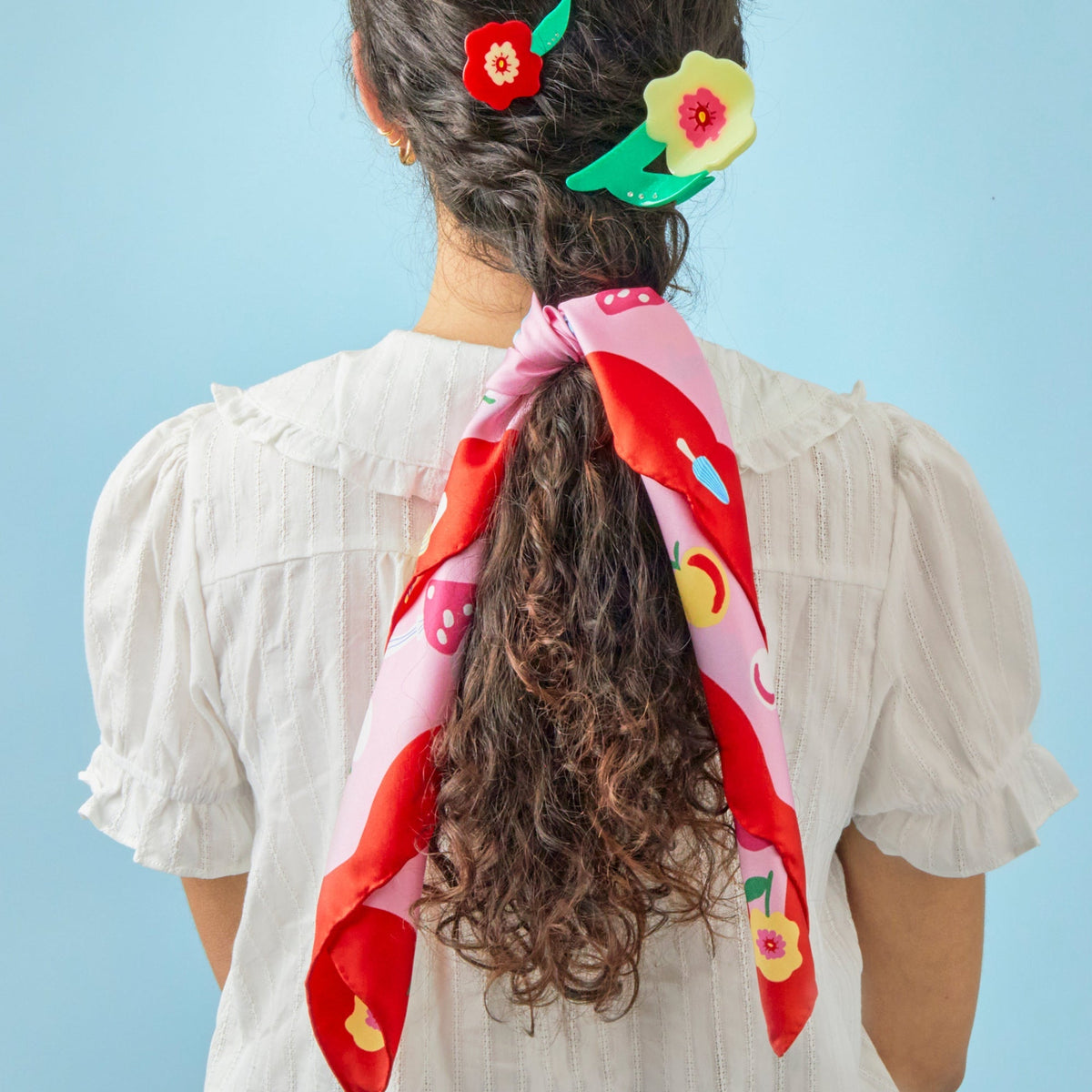 Silk square scarf tied at back of neck with red-and-pink cat, flower, and fruit print