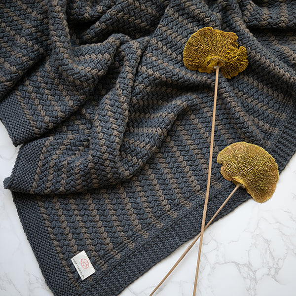 Dark blue knit throw blanket with textured weave and yellow pom-pom accents