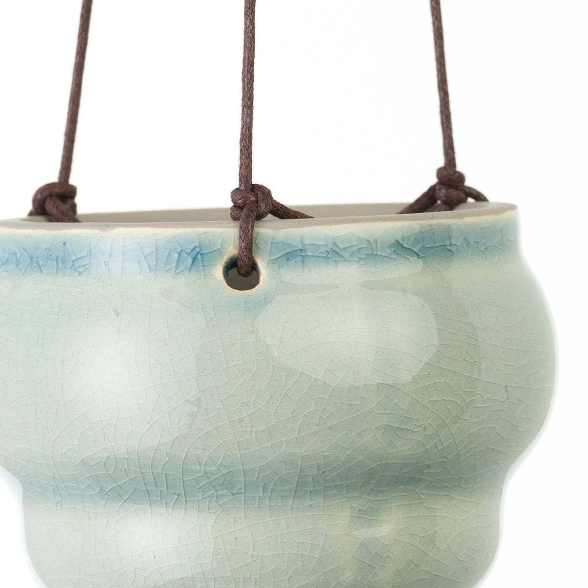Close-up of a light green hanging ceramic vase planter with knotted brown cord