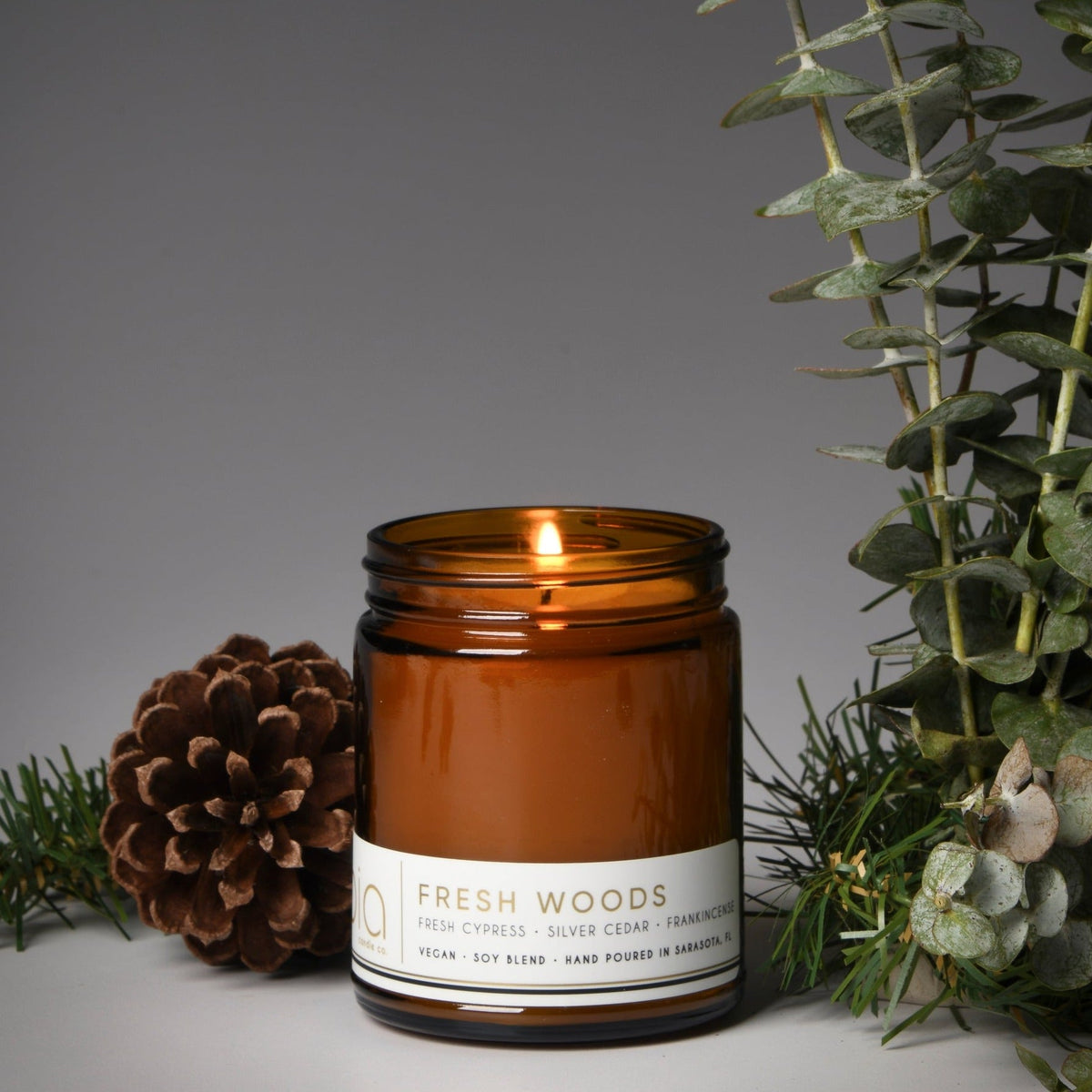 Amber glass candle jar with a visible flame and white label band on the front.
