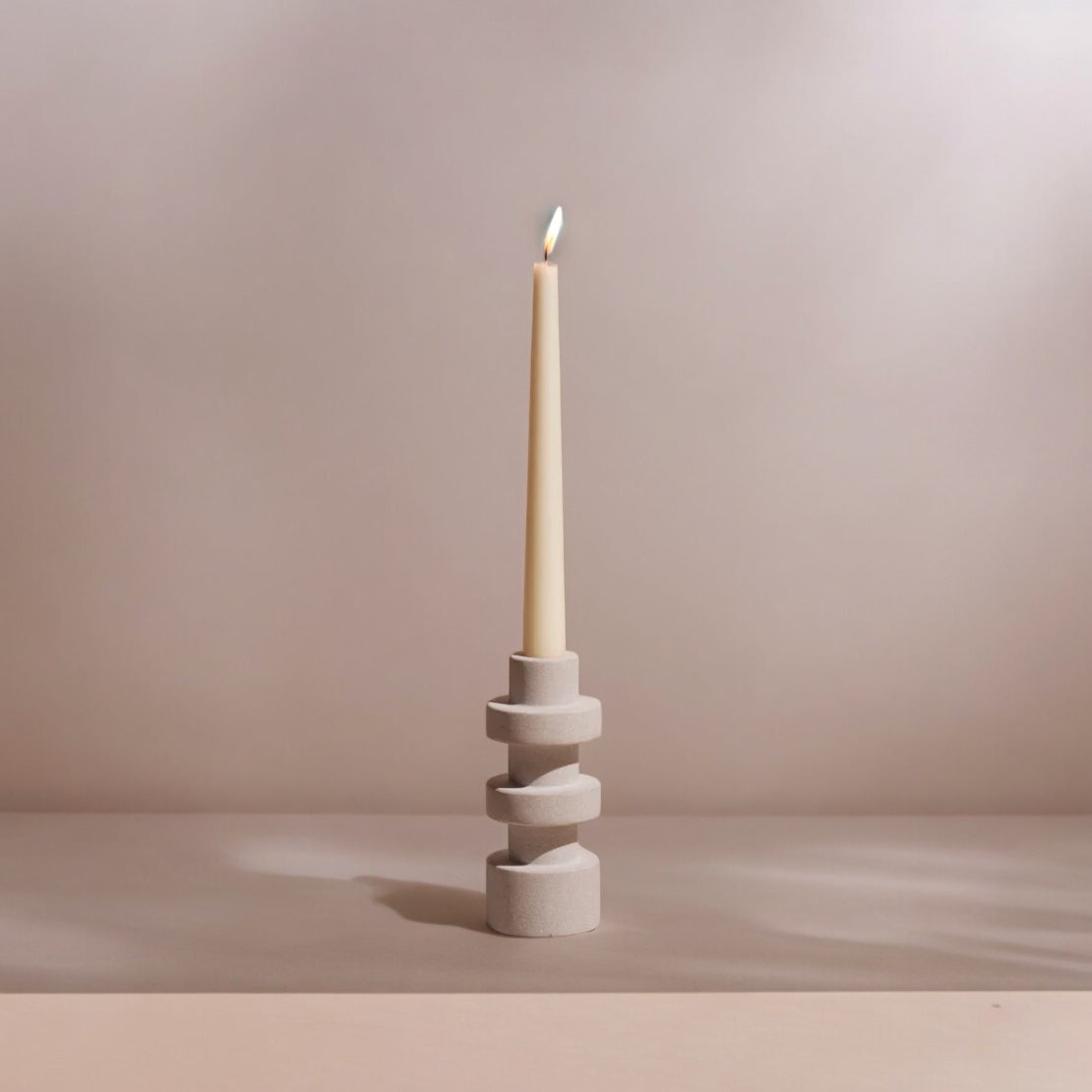 Stacked cylindrical candle holder with a white pillar candle and lit wick.