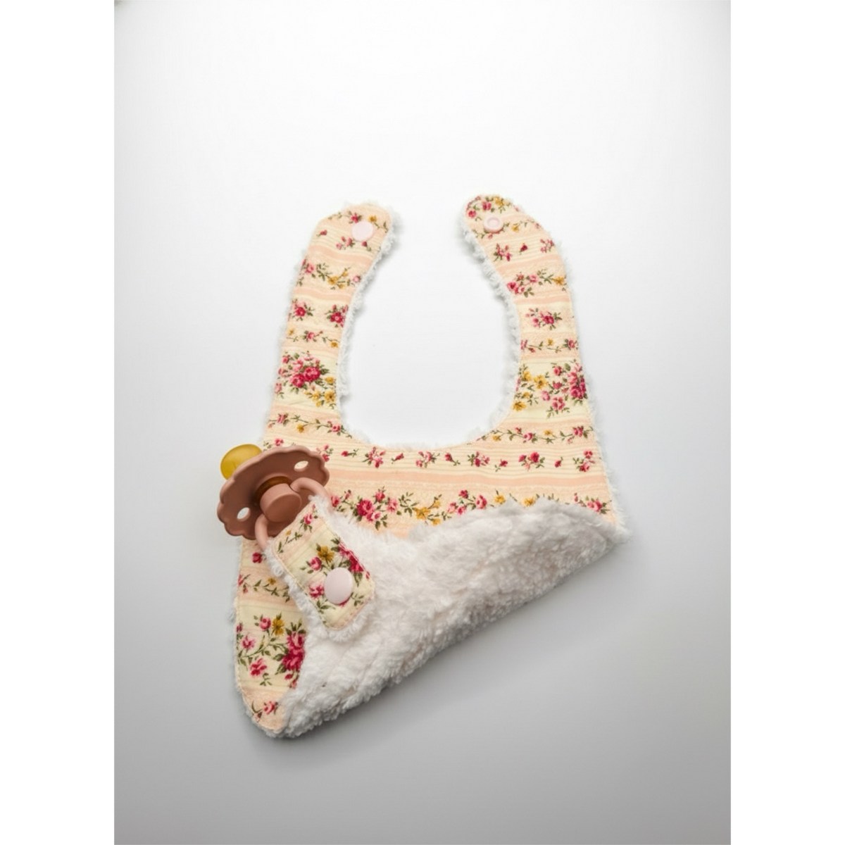 Floral pacifier bib with white fuzzy lining and mitten-shaped bottom opening