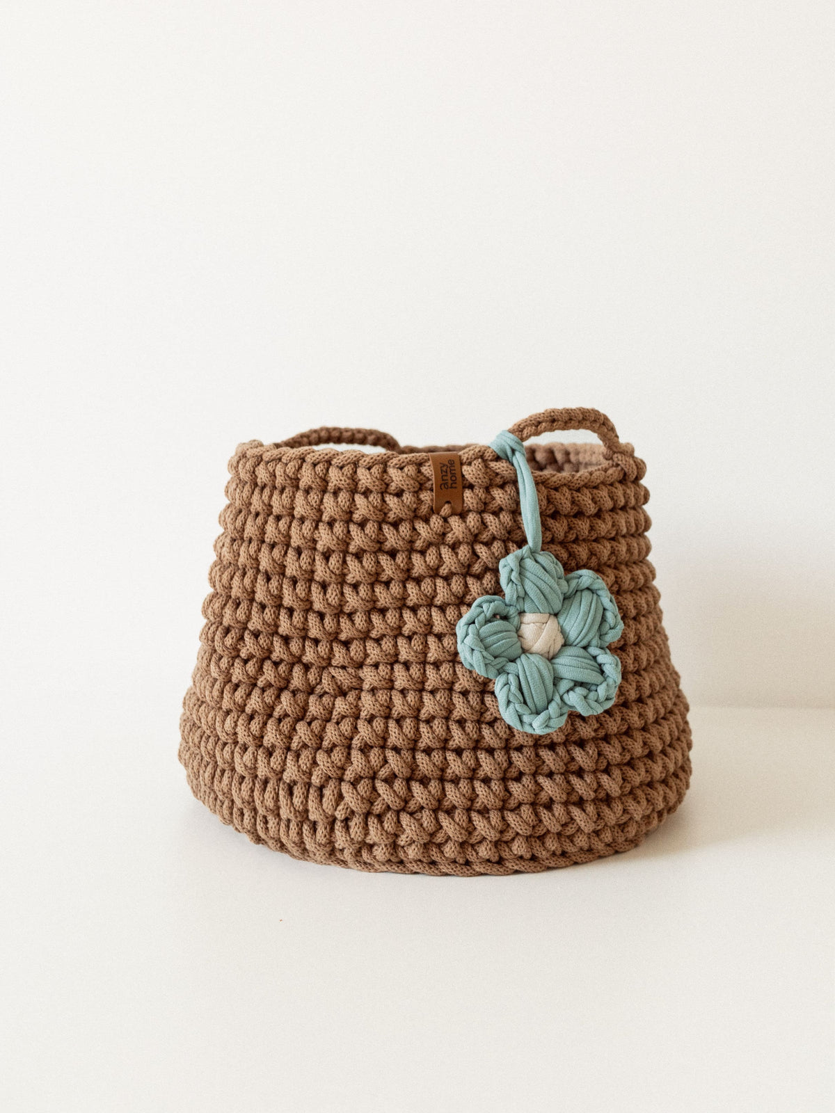 Brown crochet storage basket with teal flower applique and braided carry handles