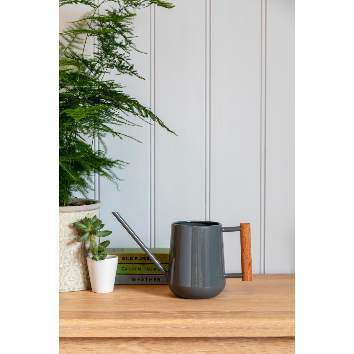 Charcoal indoor watering can with wooden handle standing on indoor shelf