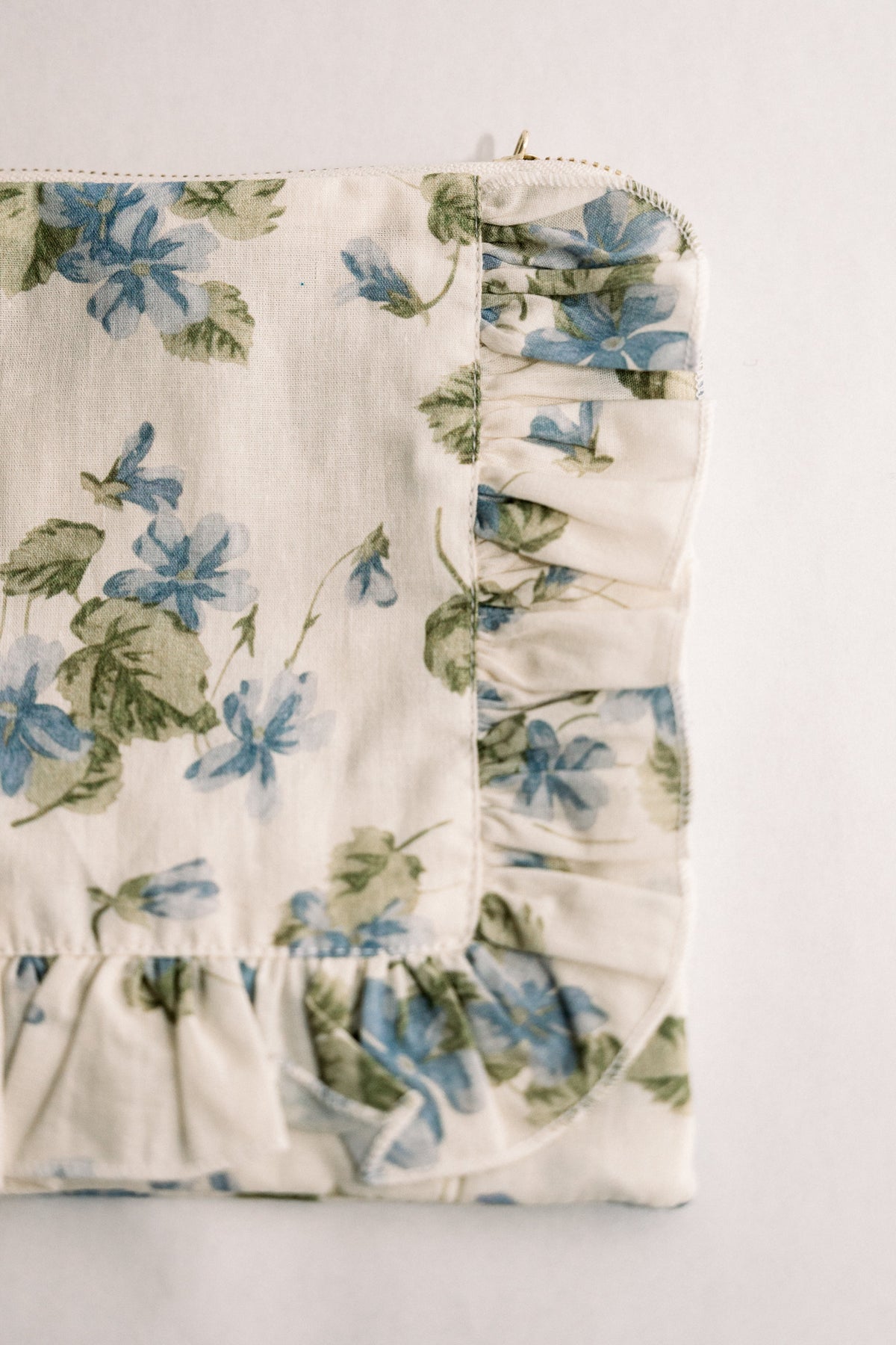 Cream floral ruffle zipper pouch with blue and green print, side view of zipper