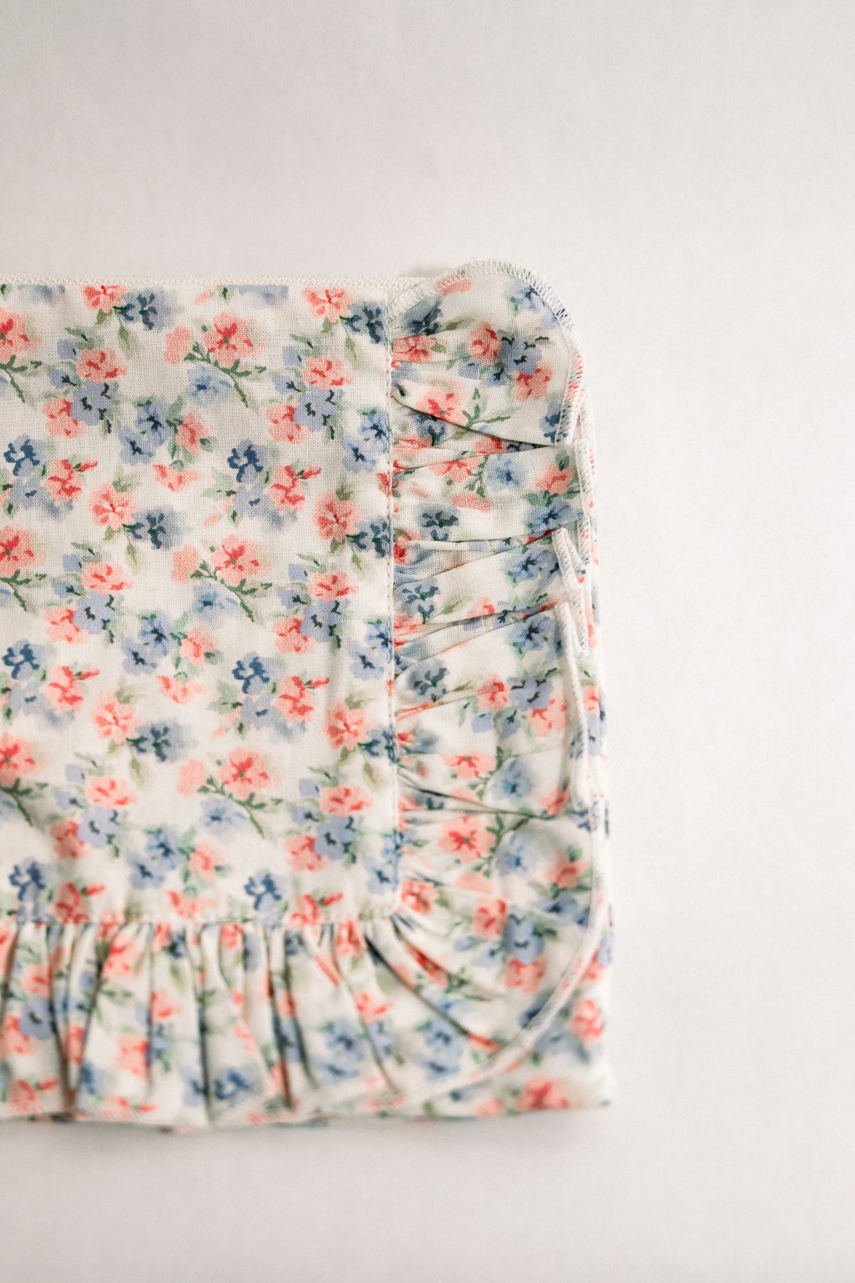 Floral ruffle zipper pouch, side view with gathered ruffle trim and light blue floral print