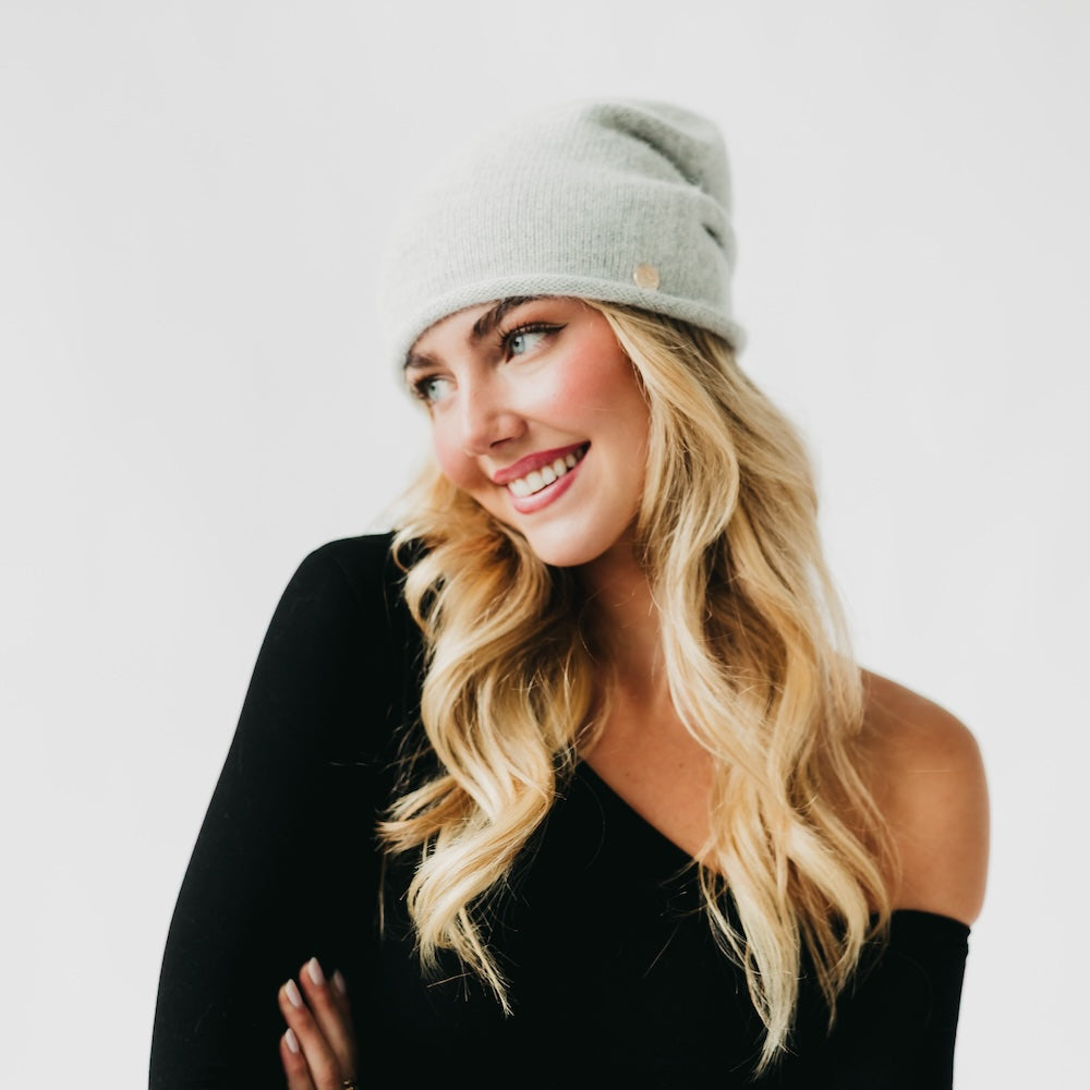 Light gray cashmere beanie with rolled cuff and small front pin, side profile.