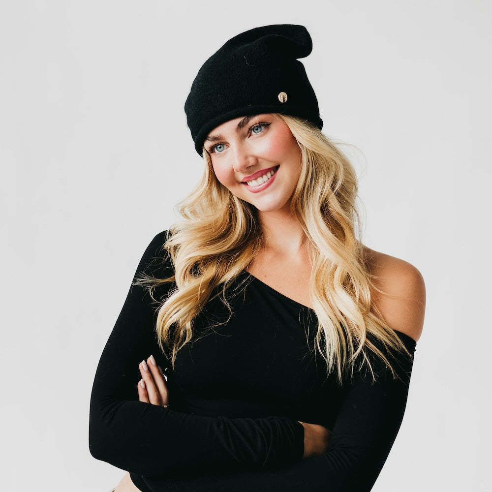 Black cashmere beanie with rolled cuff and small round pin at the front.