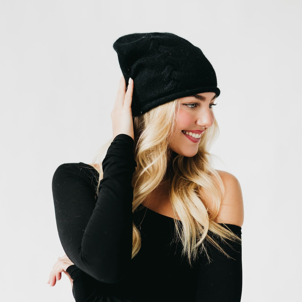 Black cashmere beanie with rolled cuff and small front pin, side view.
