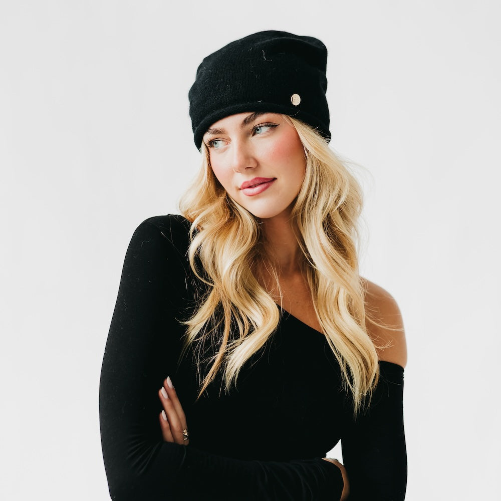 Black cashmere beanie with rolled edge cuff and small front pin detail.