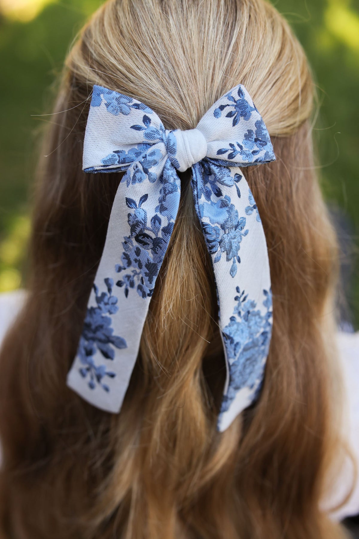 Blue floral lady hair bow tied in blonde hair, long ribbon tails