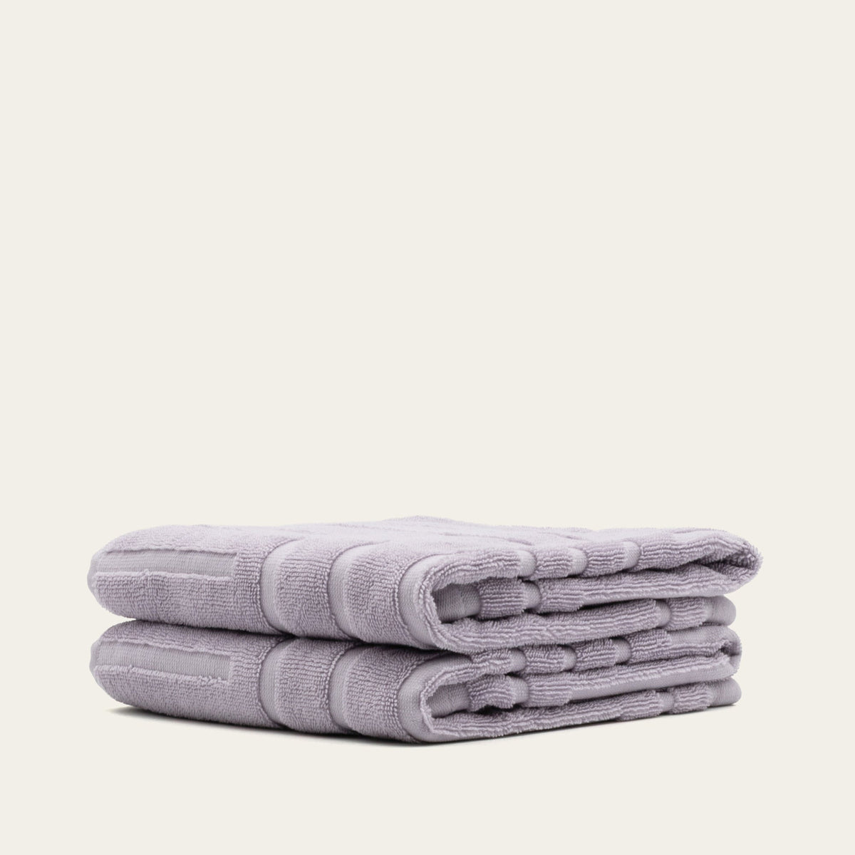Folded lilac cotton towel stack showing terry texture and stitched banding