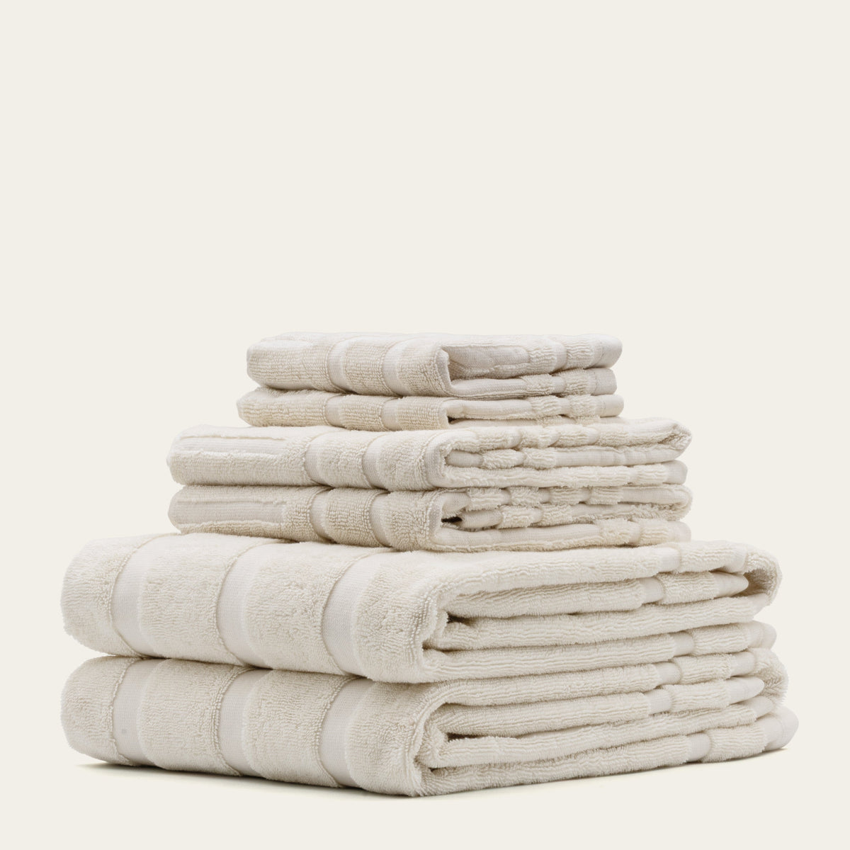 Off-white cotton towel set with stitched border bands, folded in a tall stack
