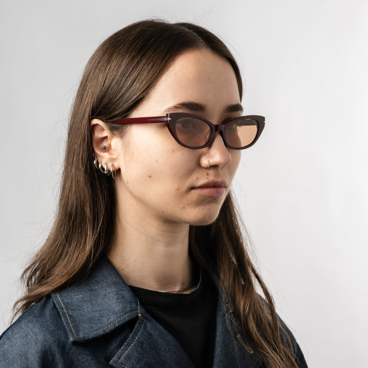 Model wearing burgundy cat-eye sunglasses with amber tinted lenses, side profile