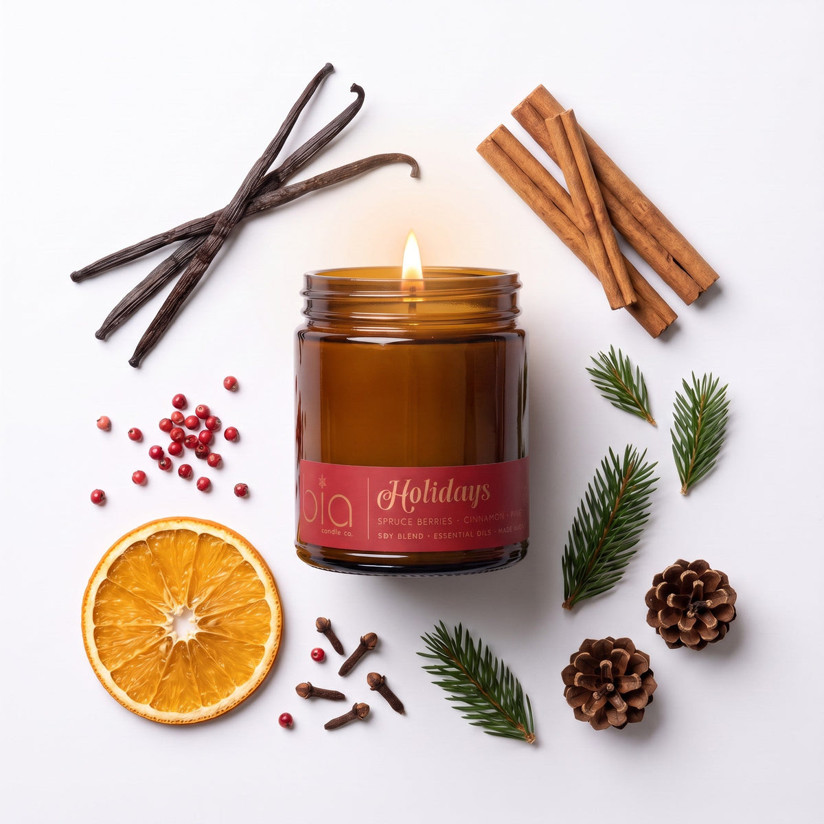 Amber candle jar with flame, with orange slice, cinnamon sticks, and cloves around.