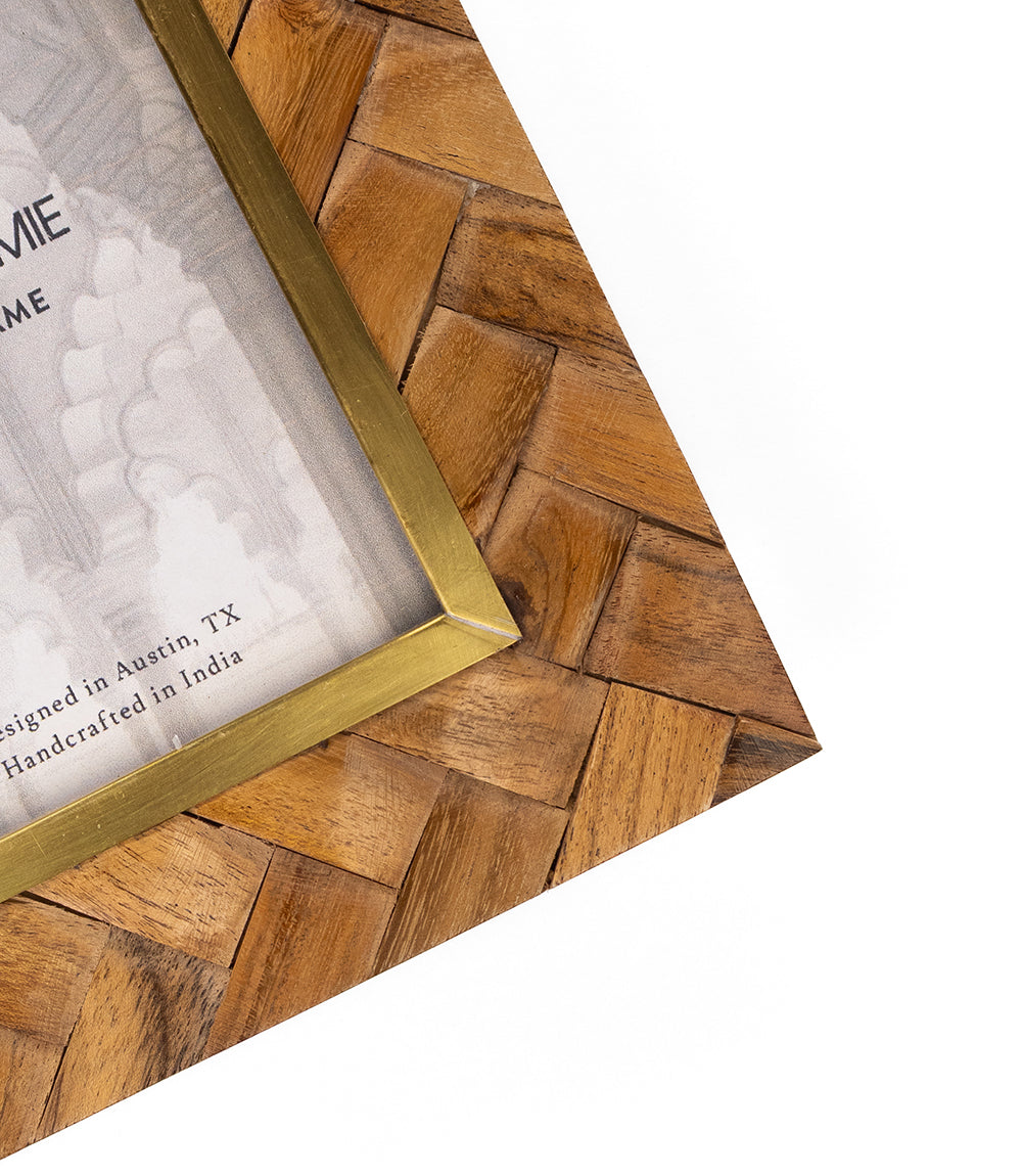 Carved wood picture frame corner with brass inlay and gold inner border, angled close-up.