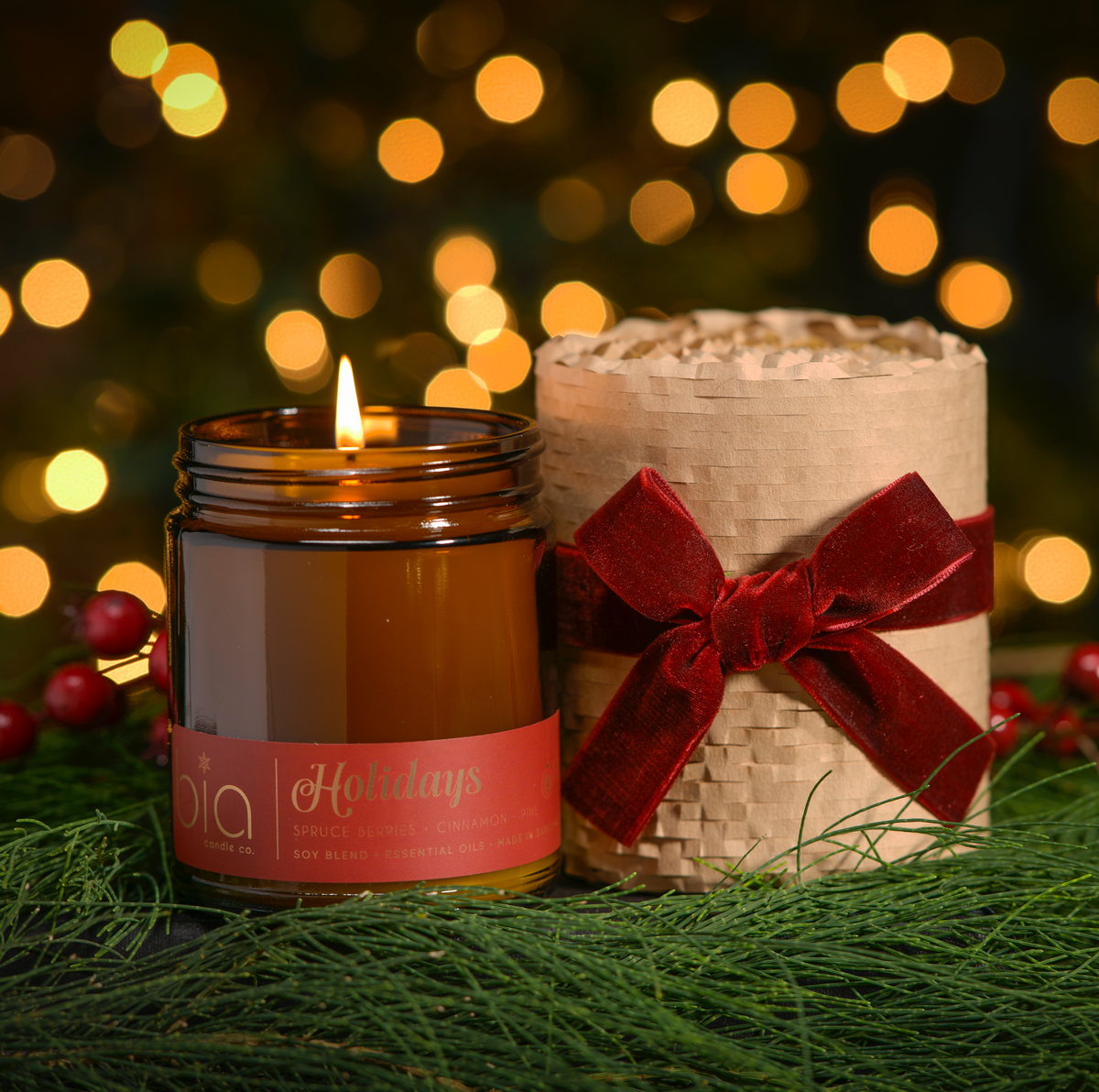 Amber candle jar with lit wick beside kraft gift wrap with red bow and ribbon