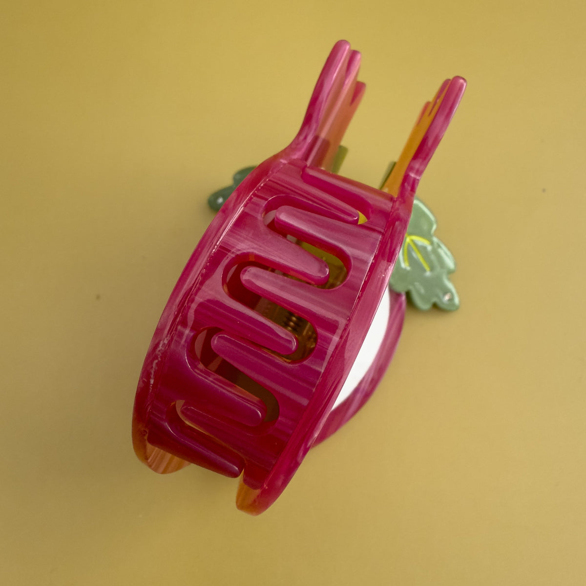 Red pomegranate hair claw side view with curved teeth and small green leaf accent